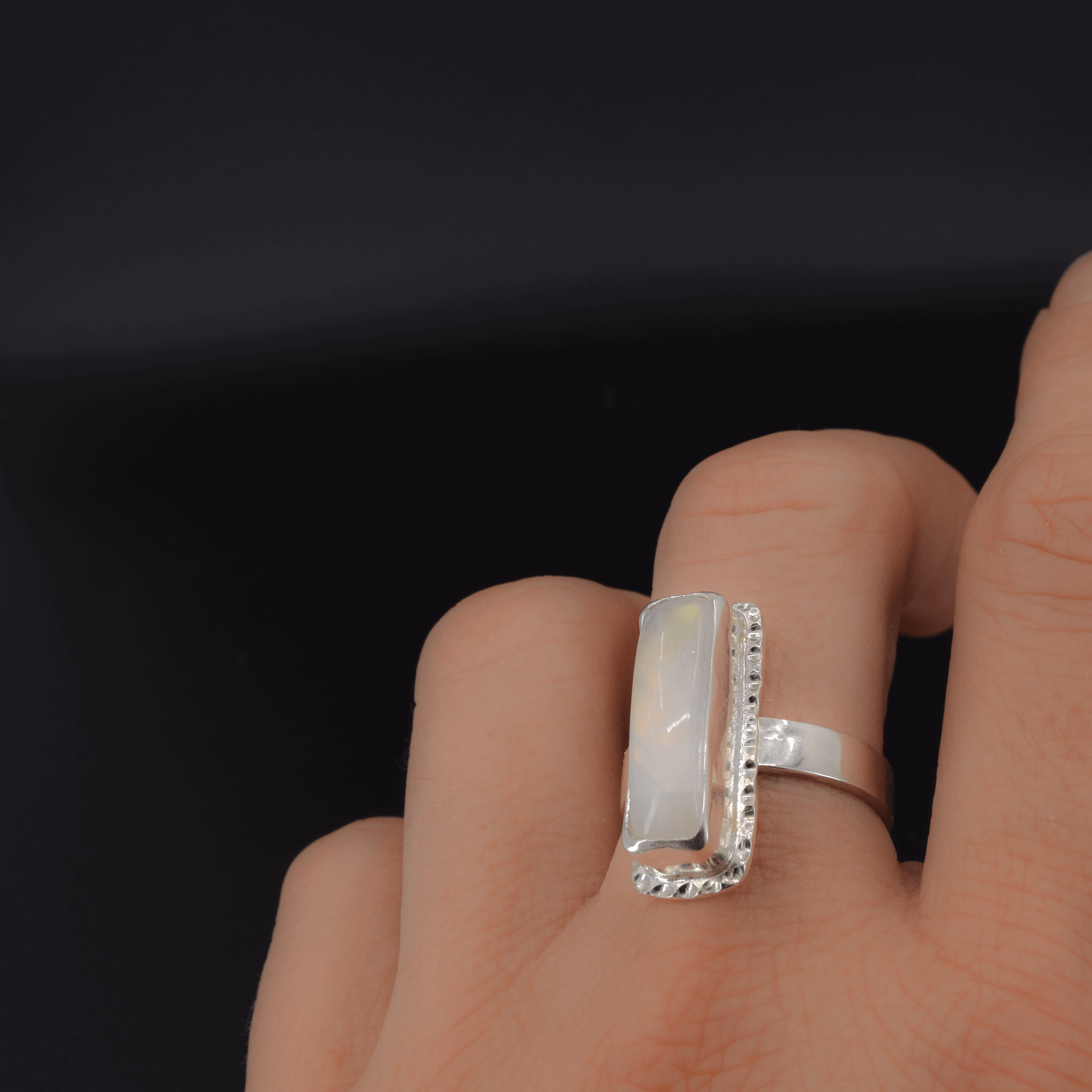 Rectangular rainbow moonstone ring shown on finger