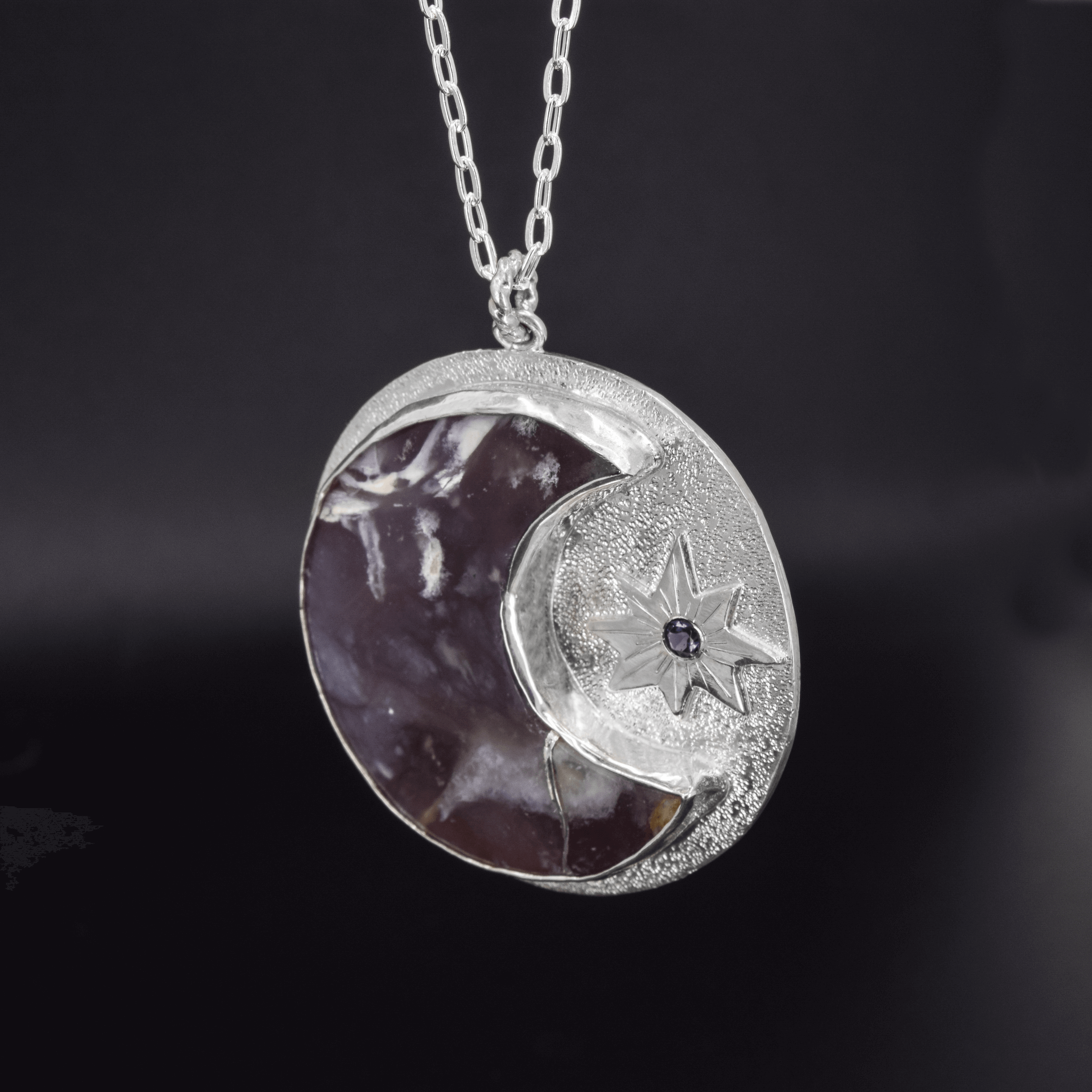 sterling silver circle pendant with an amethyst semi moon and a sun with a faceted iolite in the middle hanging on a cable chain