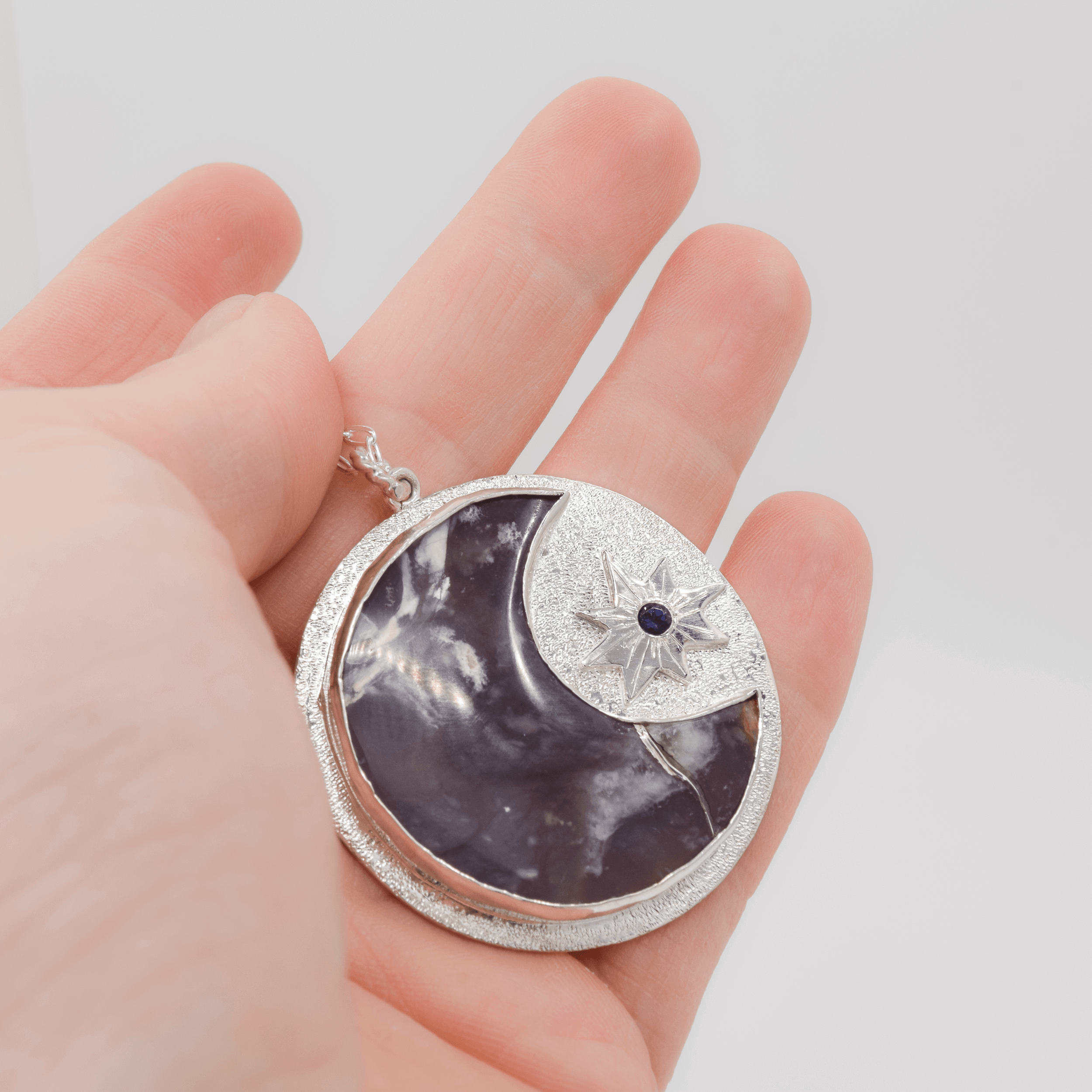 sterling silver circle pendant with an amethyst semi moon and a sun with a faceted iolite in the middle hanging on a cable chain shown for scale