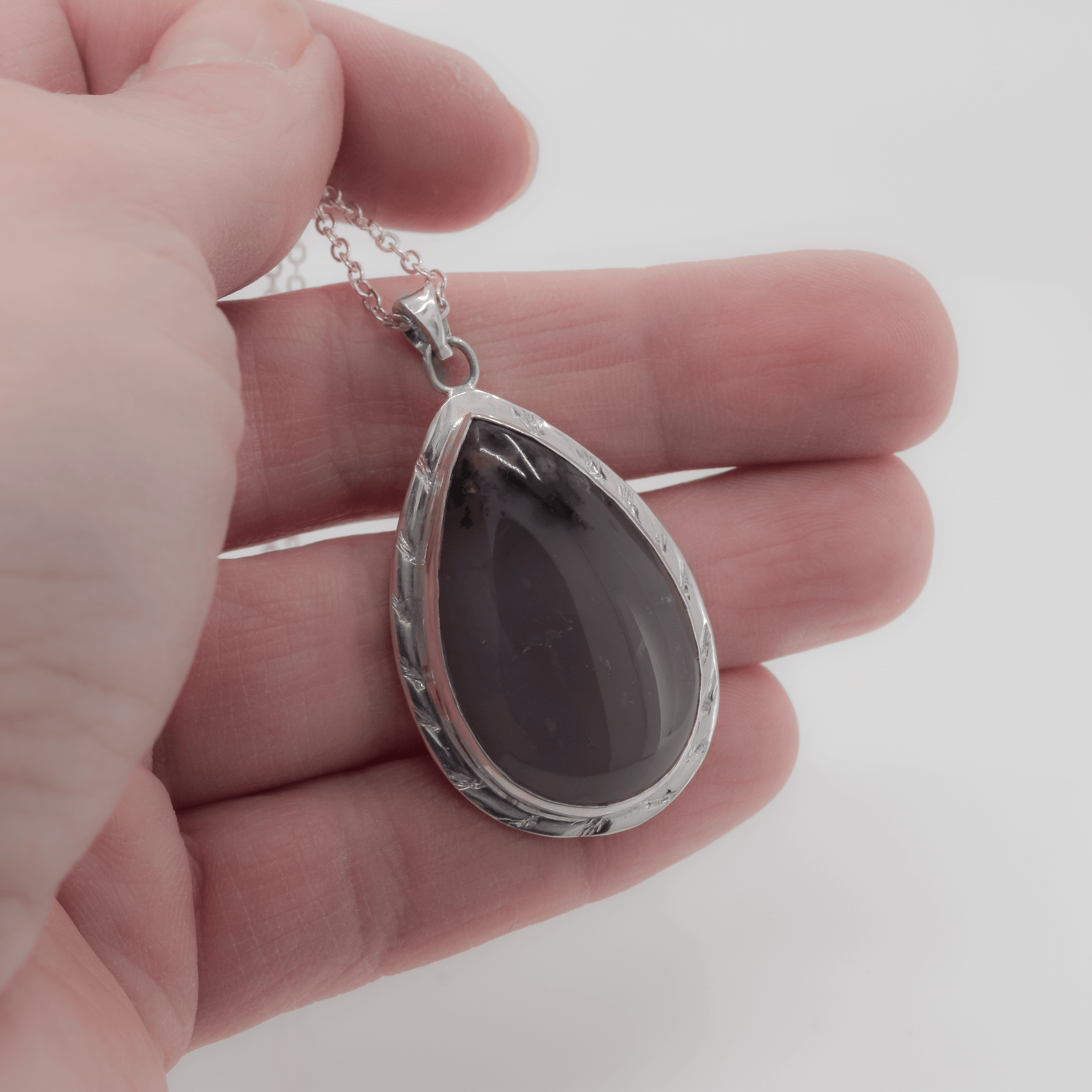 Terardrop amethyst pendant necklace with branch like texture going all around the stone. The stone also has sage inclusions at the top, giving it a more natural look. Pendant shown in hand for scale.