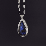 statement sterling silver pendant with a labradorite stone that has blue flashes hanging from a paperclip style chain on a black background
