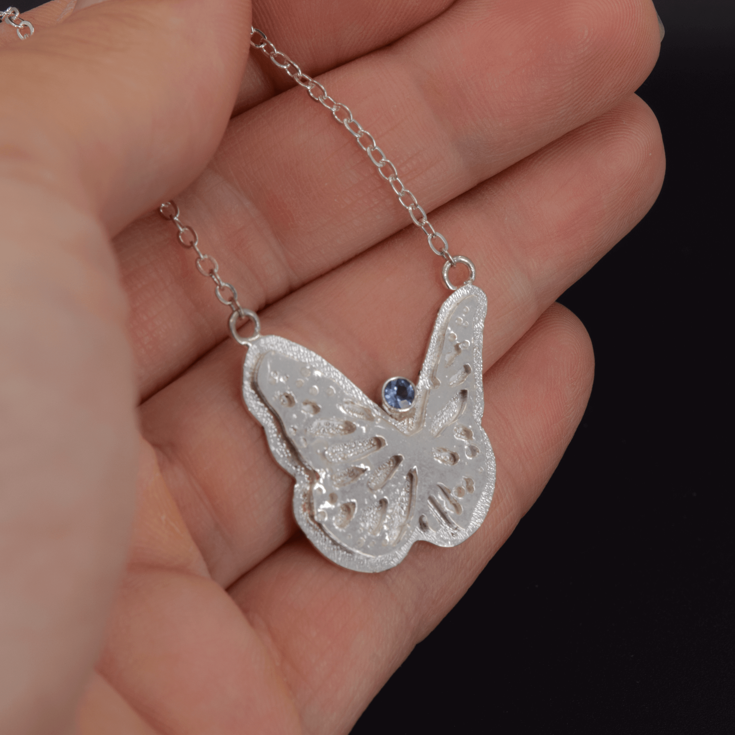 Large butterfly necklace in sterling silver with a faceted Teal Montana Sapphire round stone shown in hand for scale