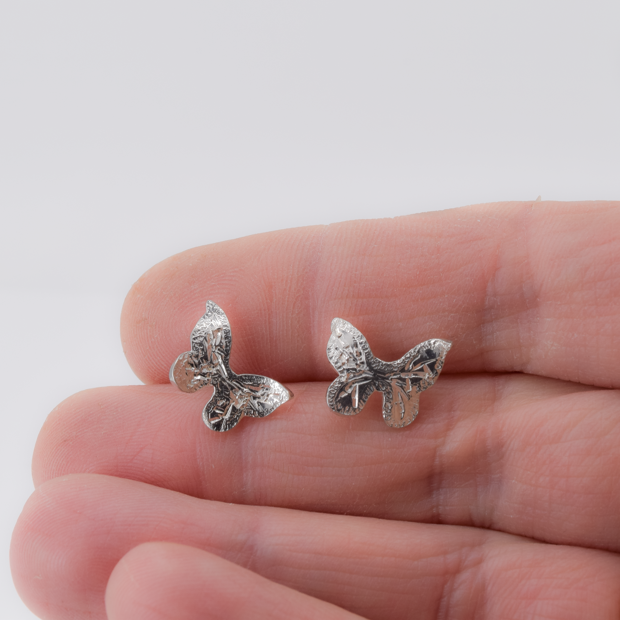 Curved hand engraved butterfly stud earrings shown in hand for scale
