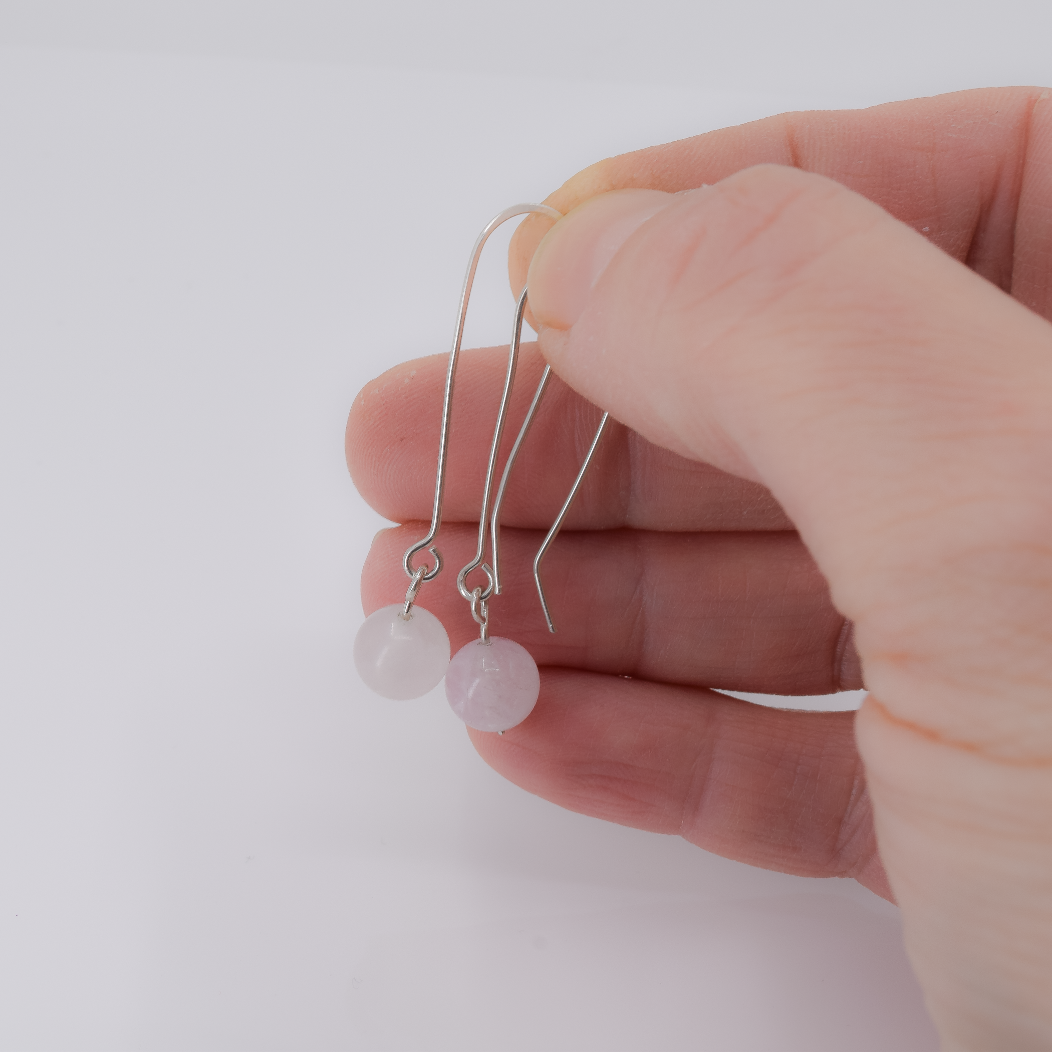 Long dangle sterling silver earrings with an 8mm round morganite bead in a light pink color shown in hand for scale