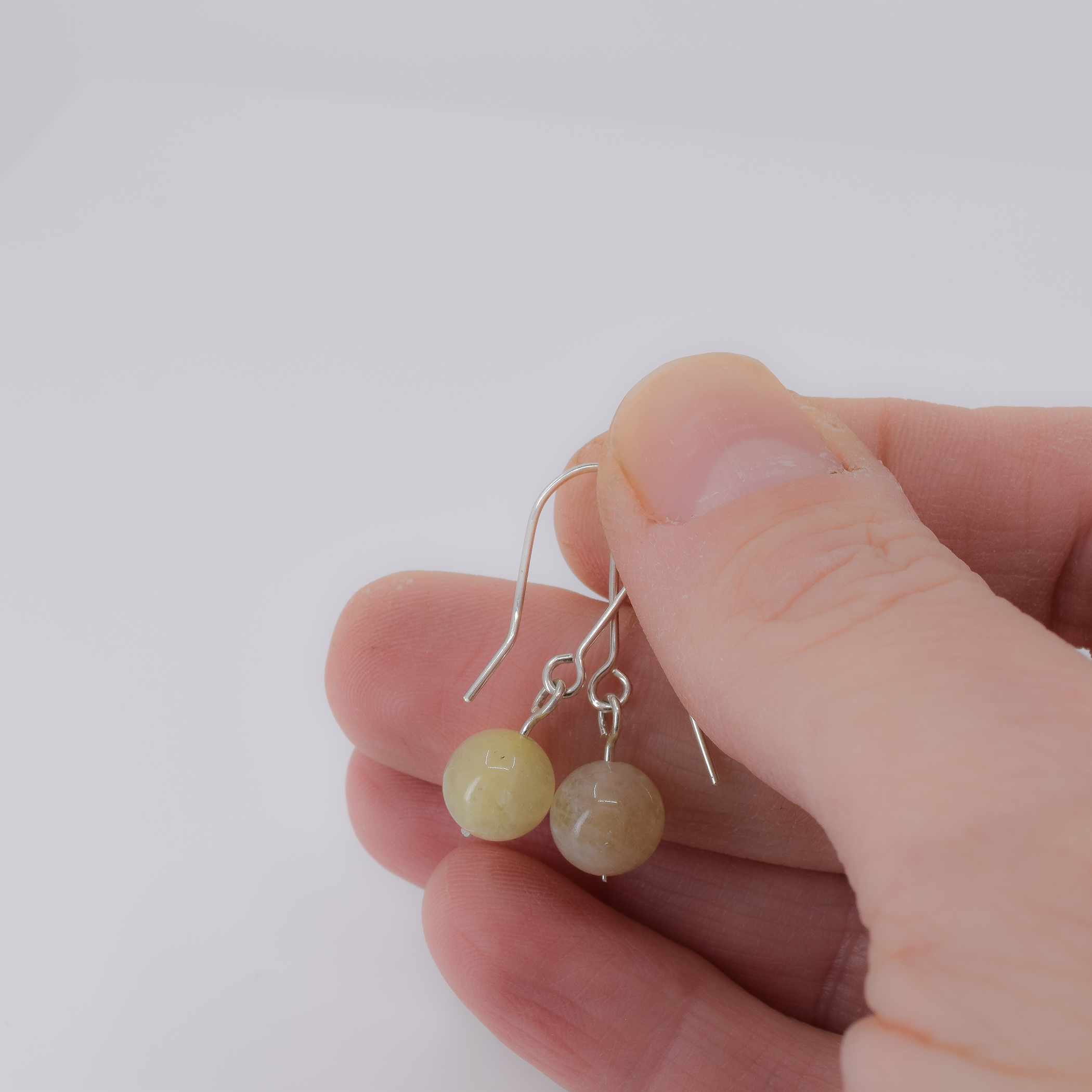 Short sterling silver dangle earrings featuring 8mm round morganite beads shown in hand for scale