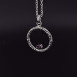 Circle of life pendant necklace in sterling silver with textured edges, featuring a rhodolite garnet faceted stone side view