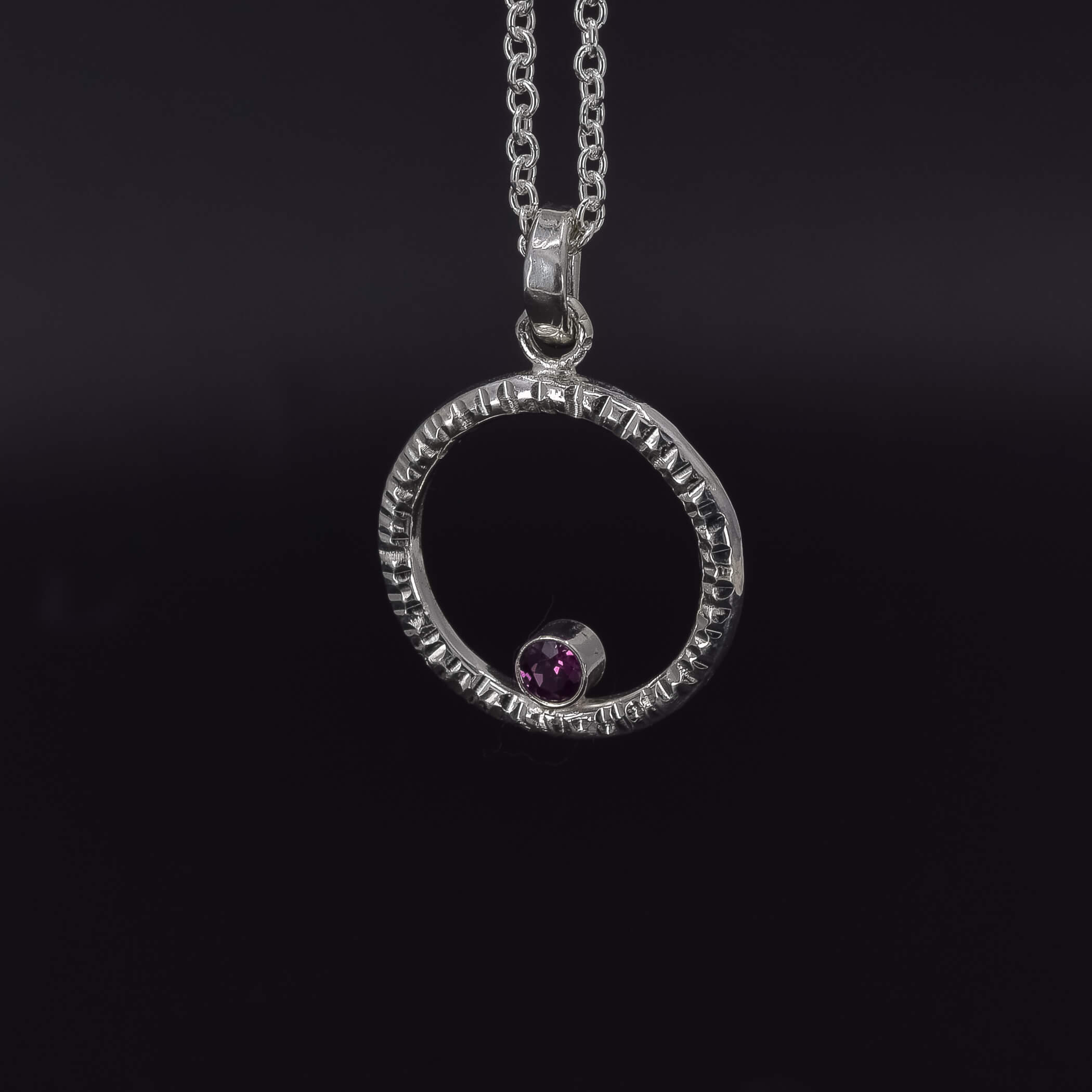 Circle of life pendant necklace in sterling silver with textured edges, featuring a rhodolite garnet faceted stone side view