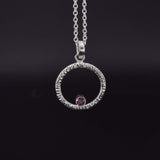 Circle of life pendant necklace in sterling silver with textured edges, featuring a rhodolite garnet faceted stone front view on black background