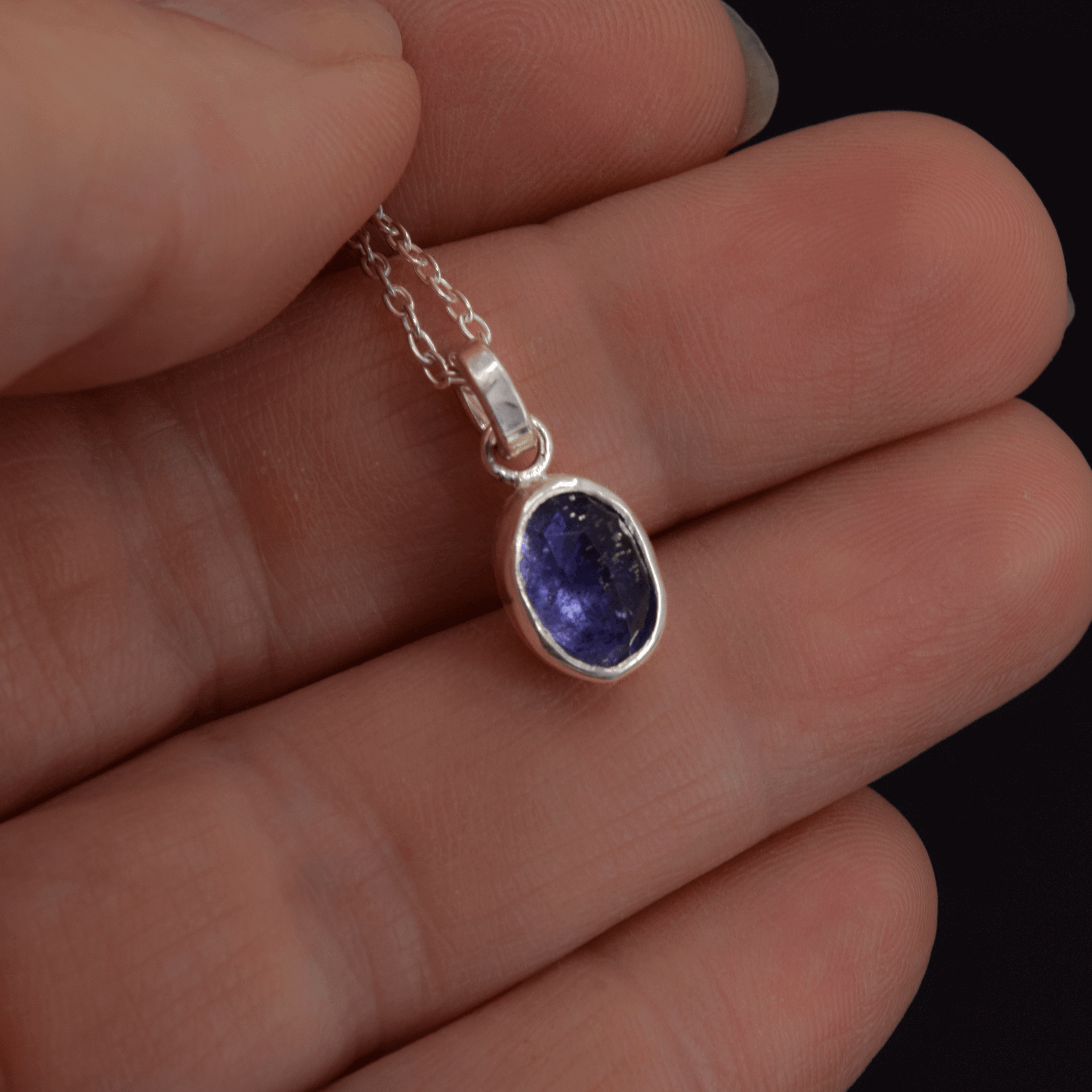 Oval rosecut iolite pendant necklace in sterling silver hanging on a cable chain shown in hand for scale