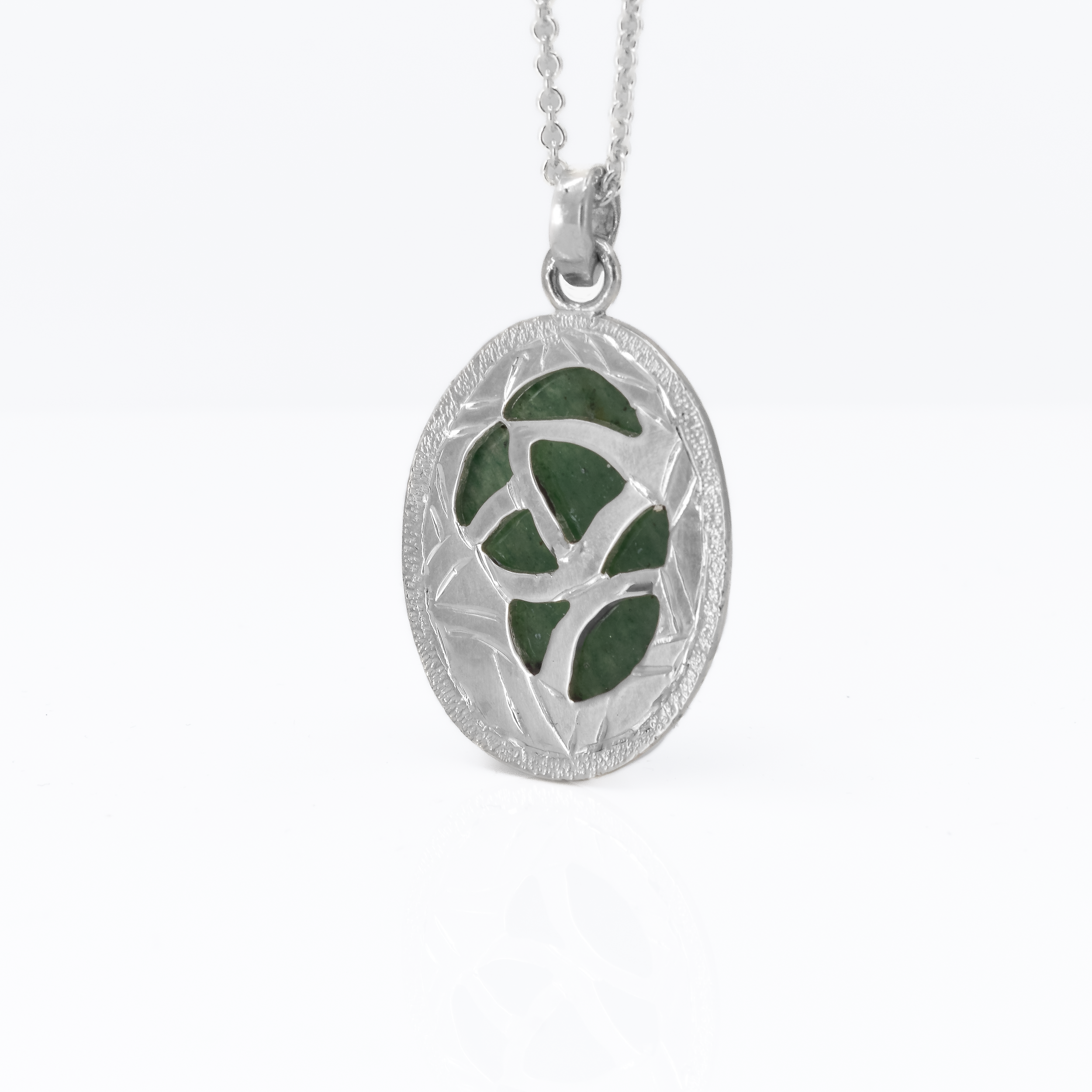 Back of an oval green jade pendant with hand engraved patterns.