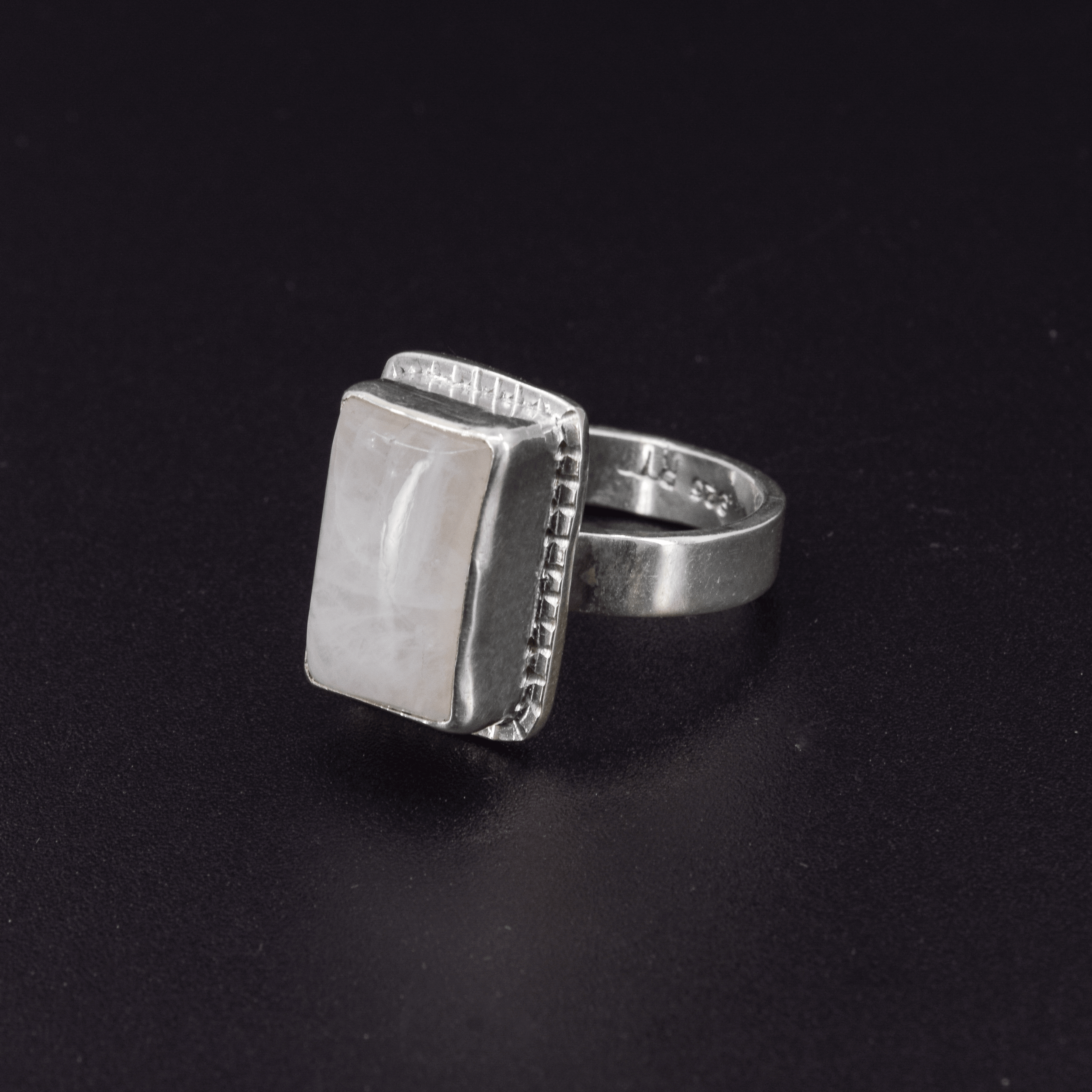 Long rectangular rainbow moonstone sterling silver ring with a hand textured border side view