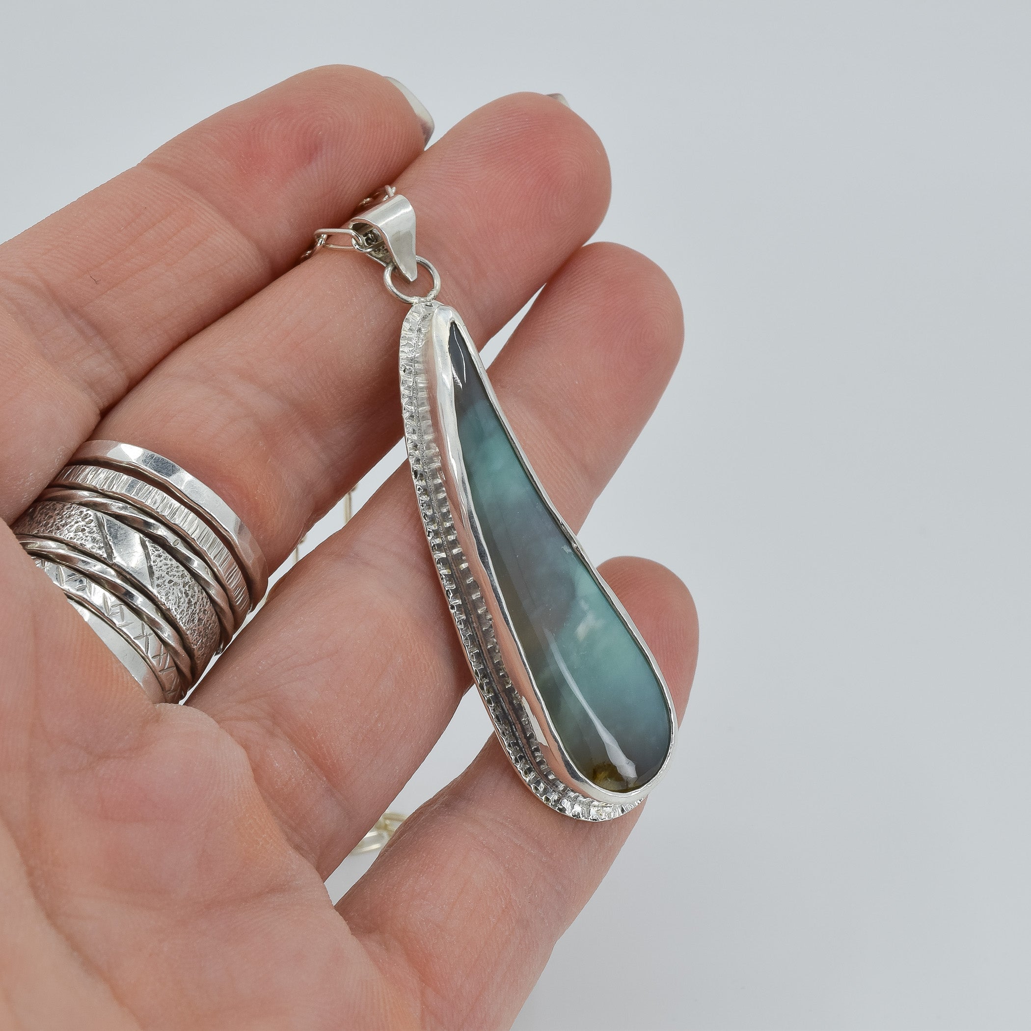 Blue opalized wood pendant necklace in sterling silver shown in hand for scale