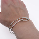 Open heart sterling silver bangle bracelet worn on wrist, along with a tree bark bangle