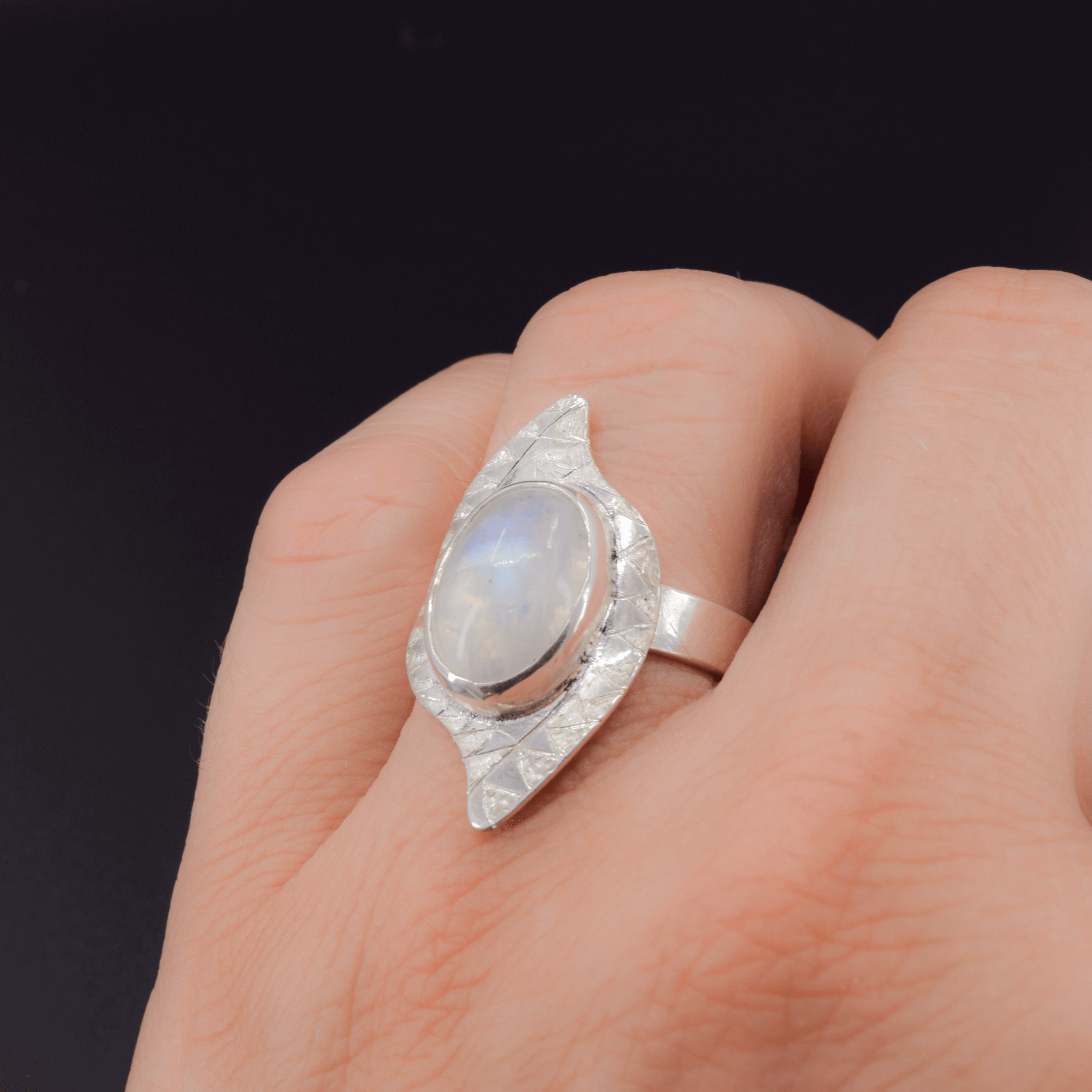 Oval rainbow moonstone sterling silver ring with a tribal style hand textured border worn on finger