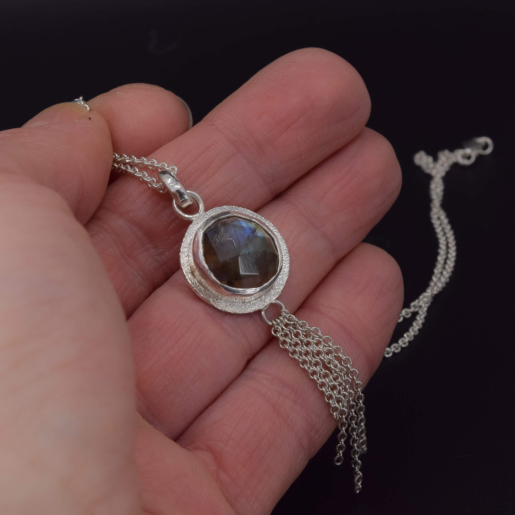  a round labradorite pendant necklace in sterling silver, which has a chain embellishment on the bottom shown in hand for scale
