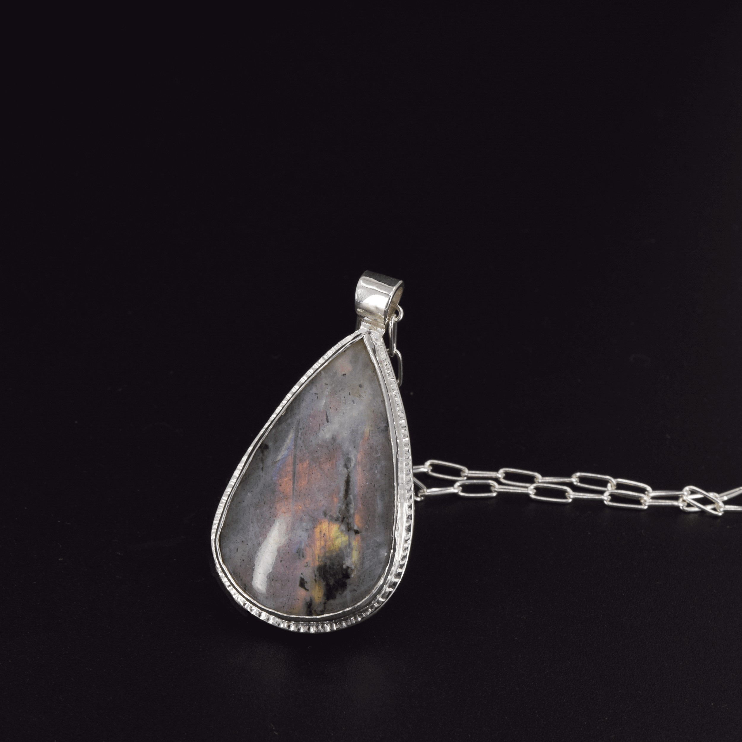 Teardrop shaped silver labradorite pendant necklace with flashes of rainbow colors set in sterling silver and hanging from a paperclip style chain 