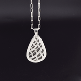 Pierced and hand textured and engraved back side of a teardrop shaped silver labradorite pendant set in sterling silver, with a hand textured decorative border surrounding the stone and hanging from a paperclip style chain