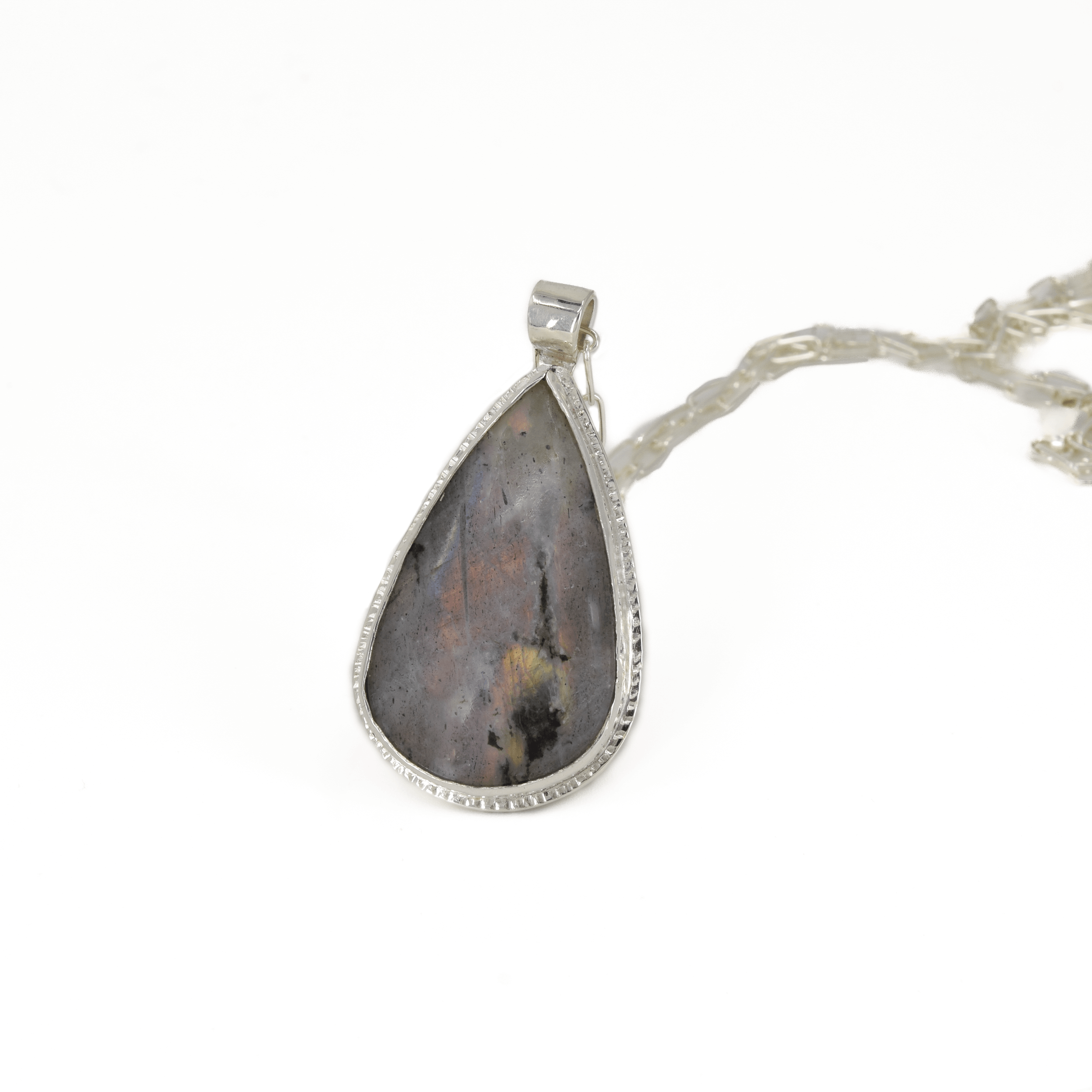 Teardrop shaped silver labradorite pendant with flashes of rainbow colors set in sterling silver, with a hand textured decorative border surrounding the stone and hanging from a paperclip style chain