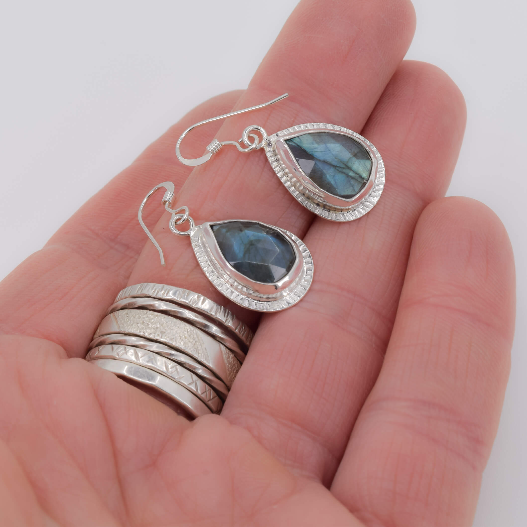 Teardrop shaped labradrotie drop earrings set in sterling silver with a detailed border adorning the edges of the stones shown in hand for scale