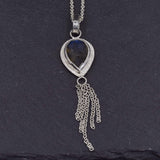 view of a teardrop labradorite set in sterling silver with a dainty chain embellishment hanging at the bottom  on a slate background
