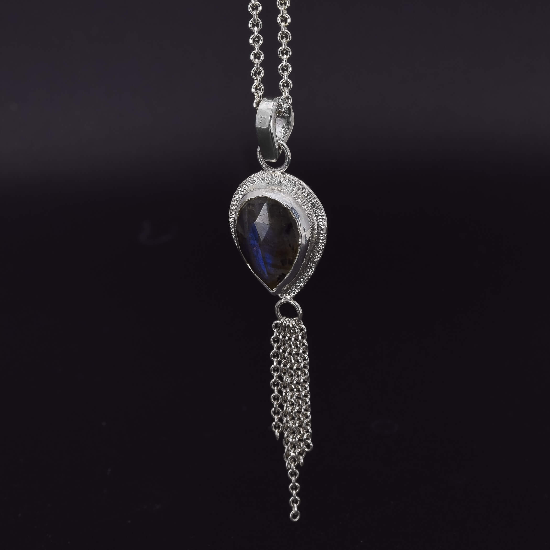 side view of a teardrop labradorite set in sterling silver with a dainty chain embellishment hanging at the bottom 