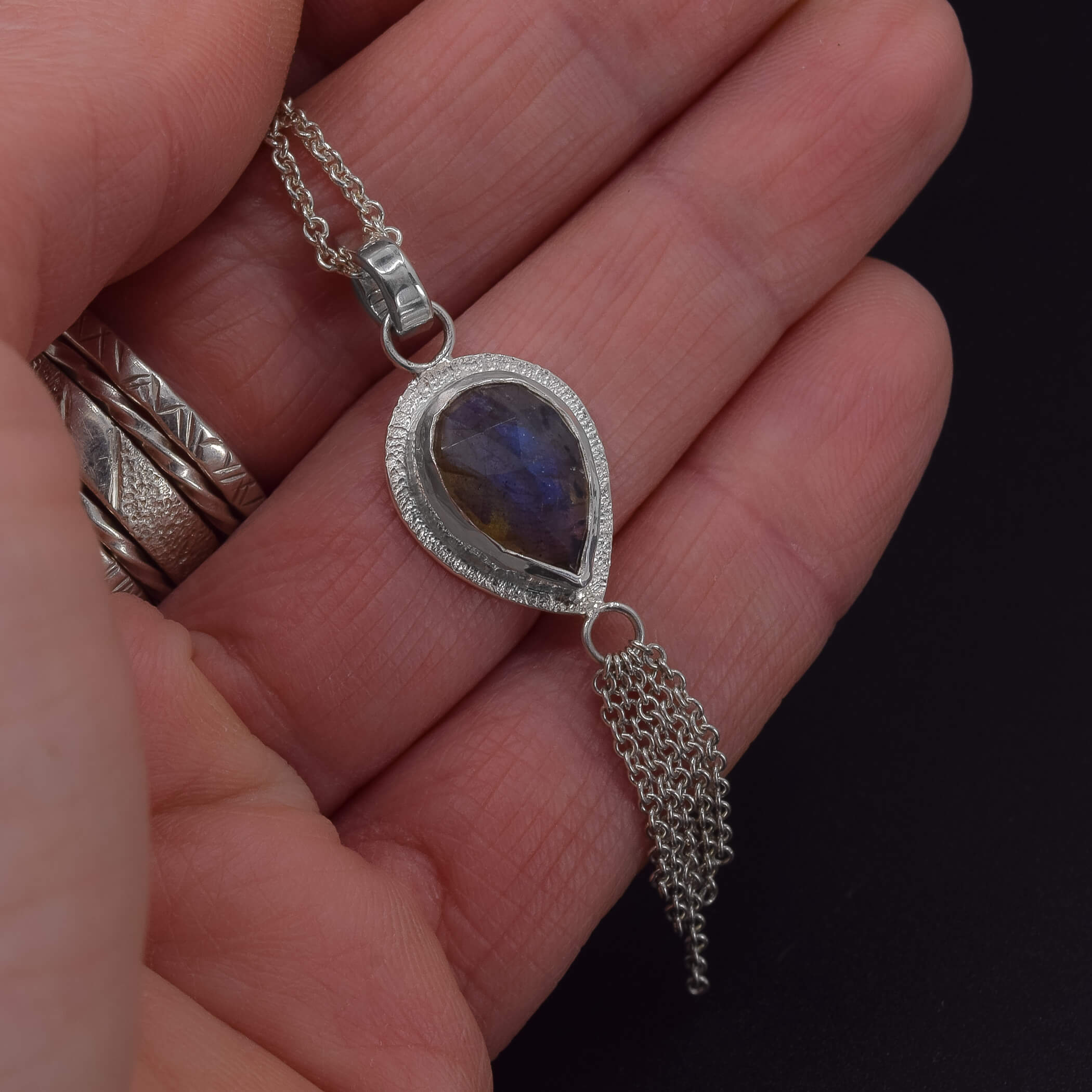 Teardrop labradorite set in sterling silver with a dainty chain embellishment hanging at the bottomTeardrop labradorite set in sterling silver with a dainty chain embellishment hanging at the bottom shown in hand for scale