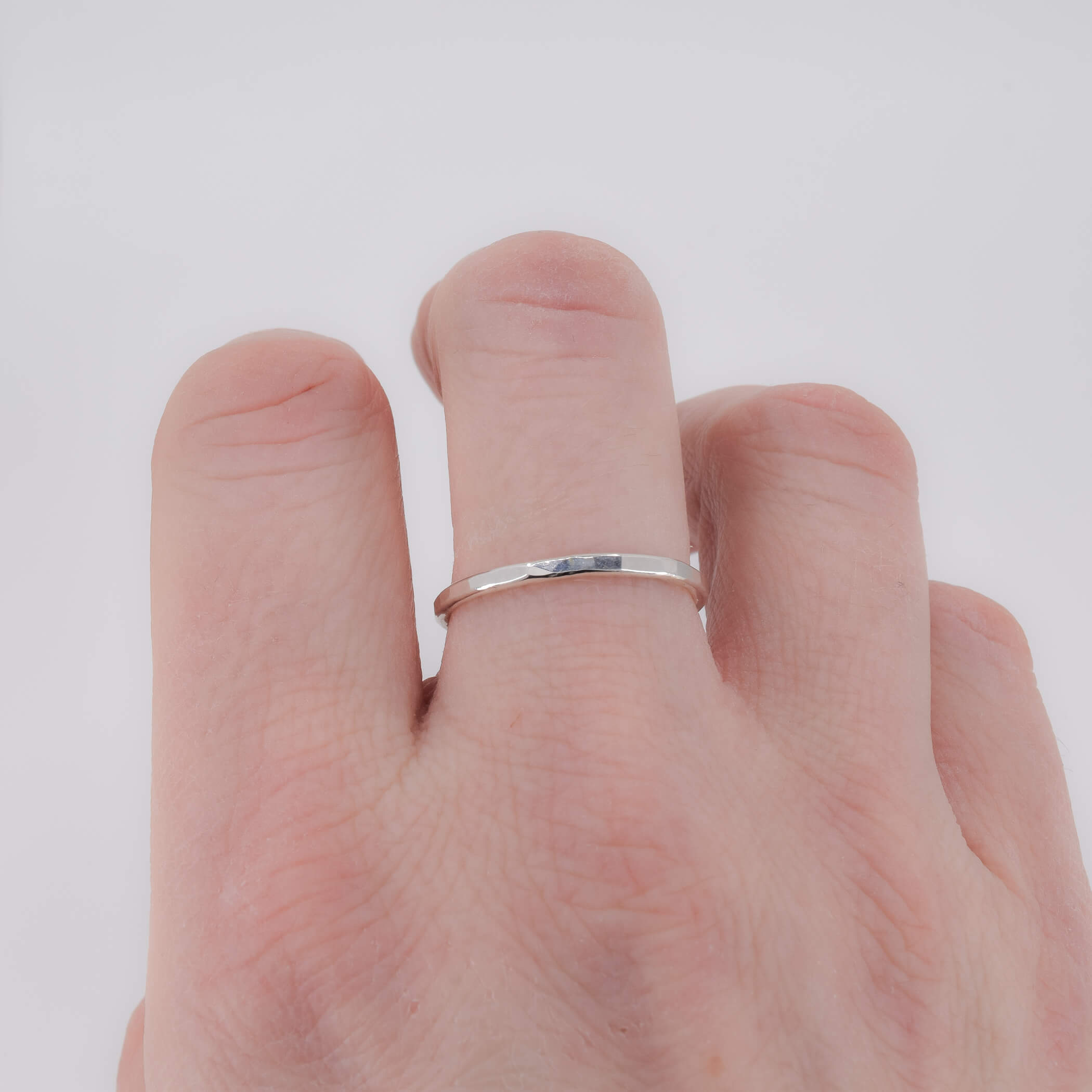 Thin faceted sterling silver stacking ring shown on finger for scale 