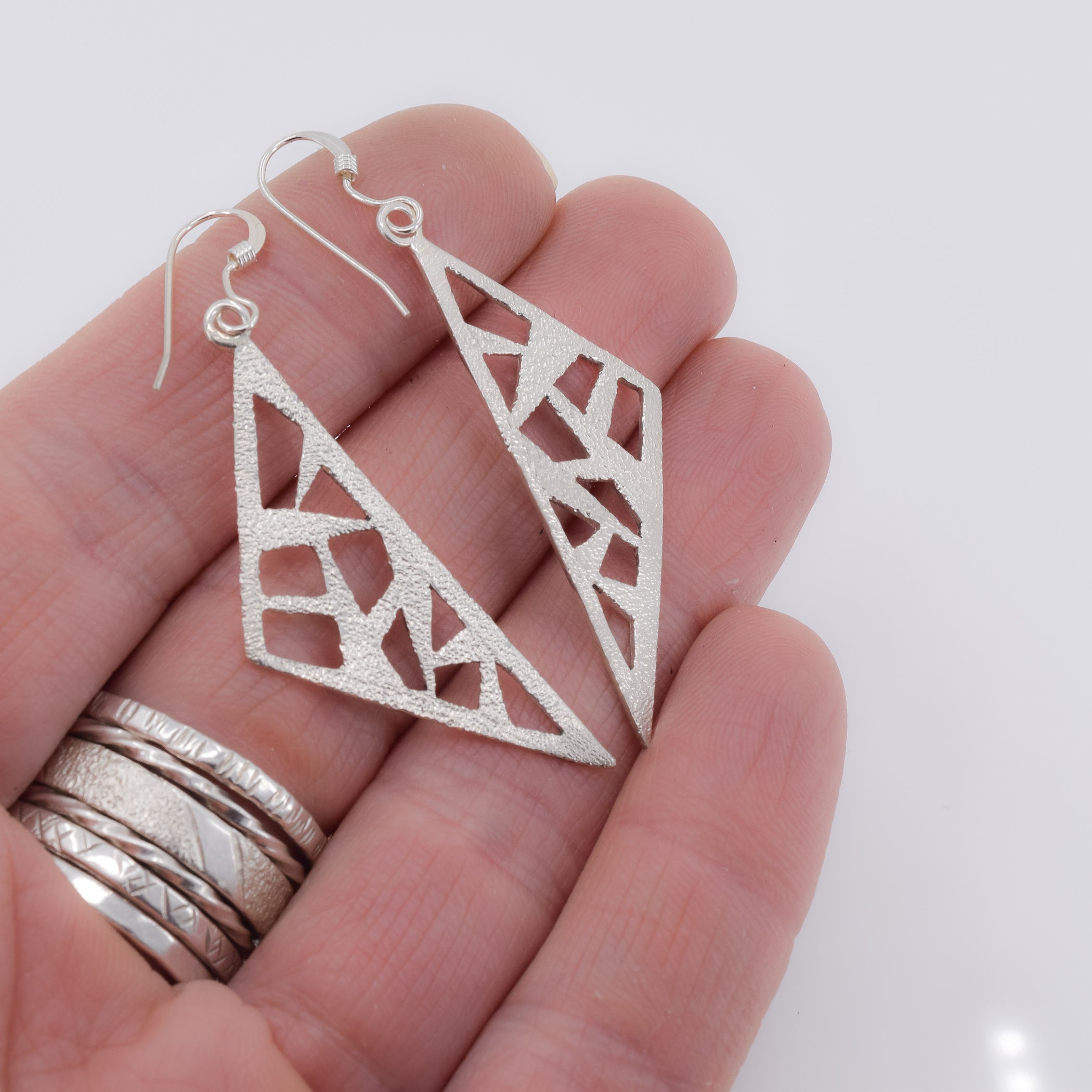 Triangle dangle earrings in sterling silver pierced with a modern design shown in hand