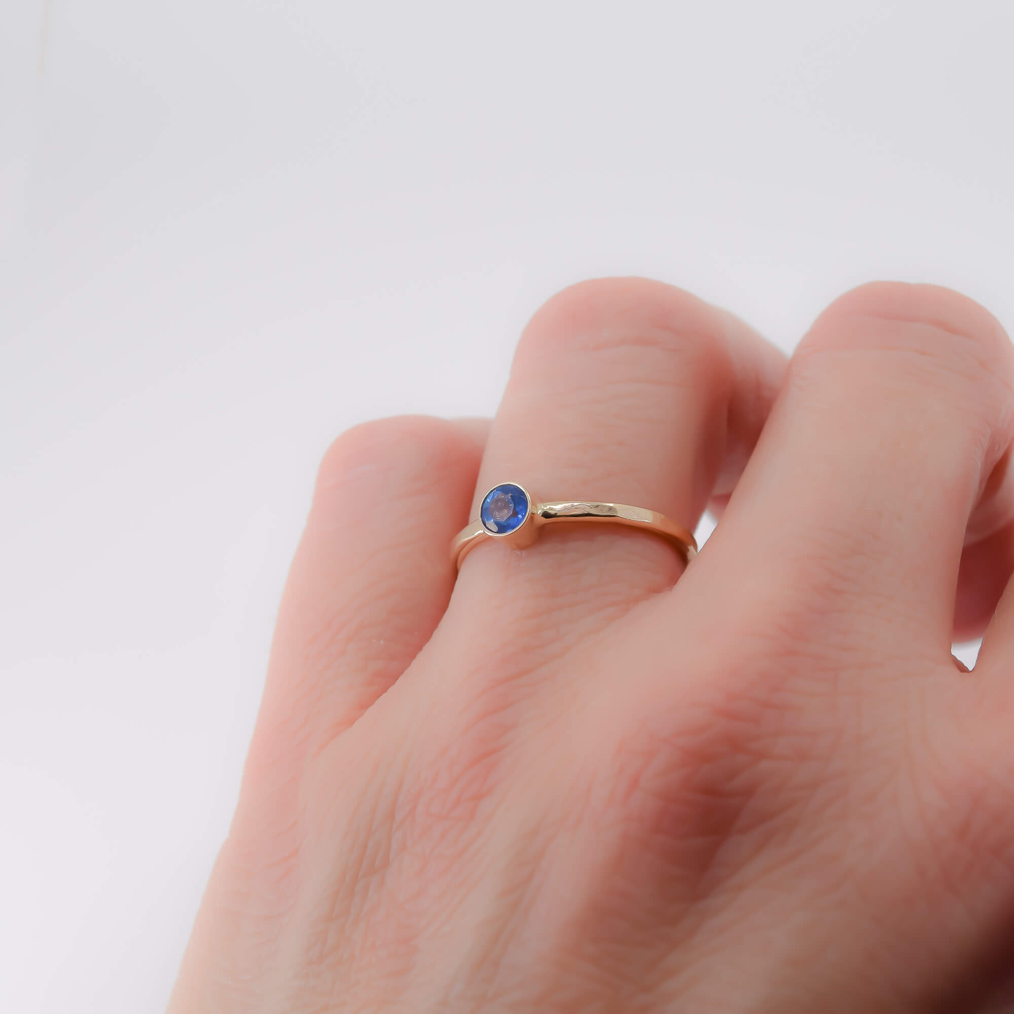 14K yellow gold thin stackable ring with ice blue topaz stone modeled on finger for scale